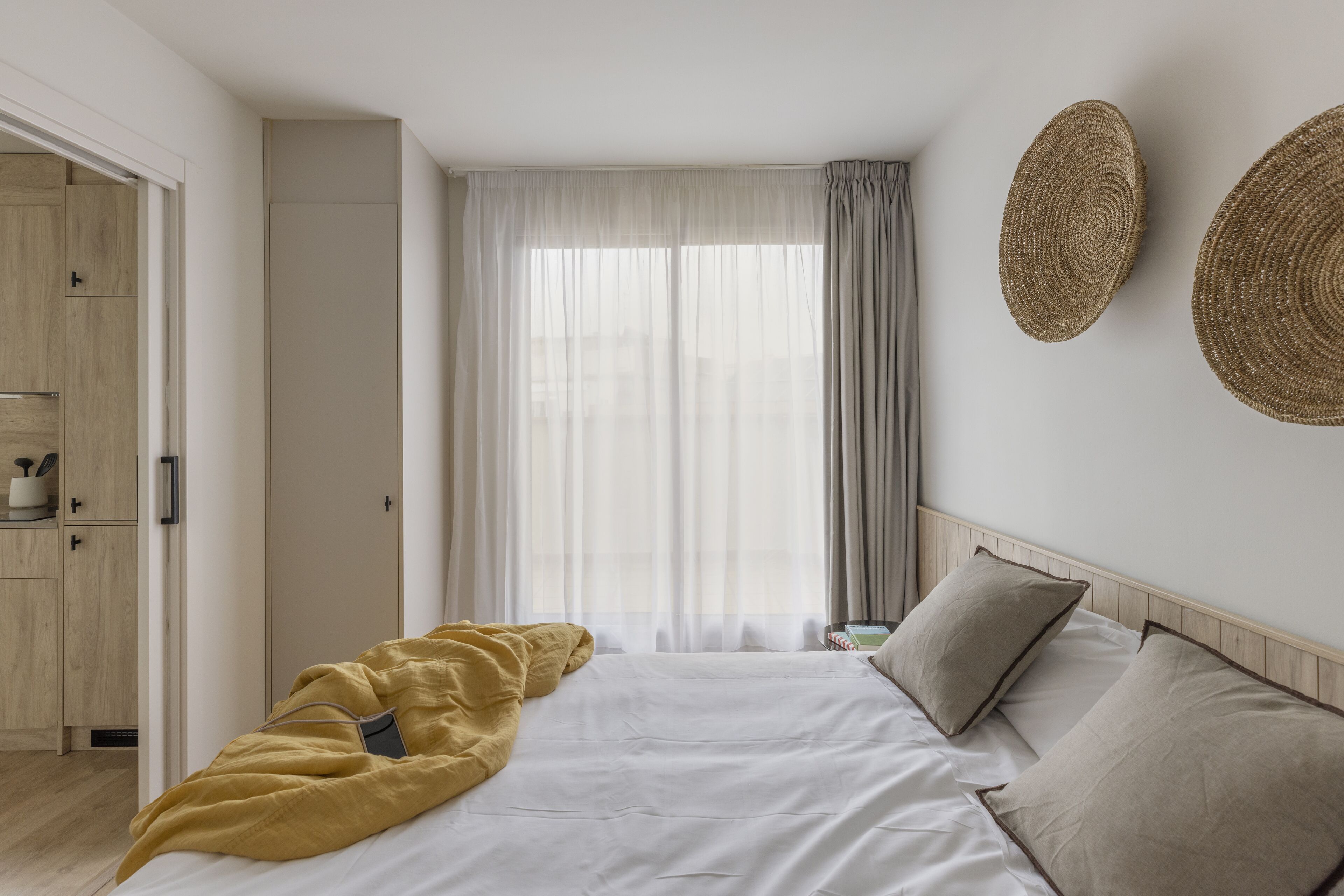 A bedroom with a bed, a wardrobe, a window with curtains, and two wall-mounted woven baskets.