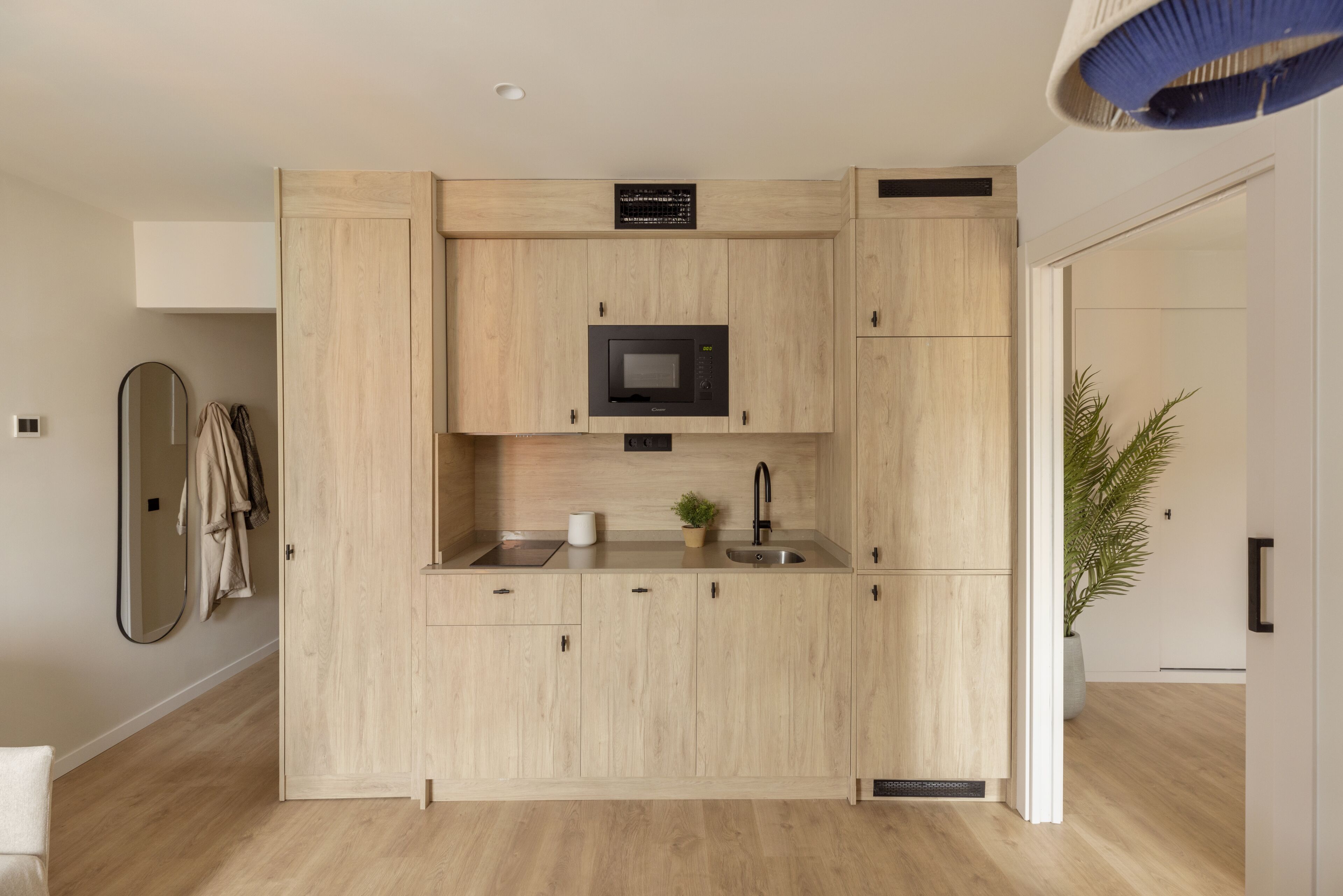 Una cocina moderna con muebles de madera clara, microondas integrado y un lavamanos.