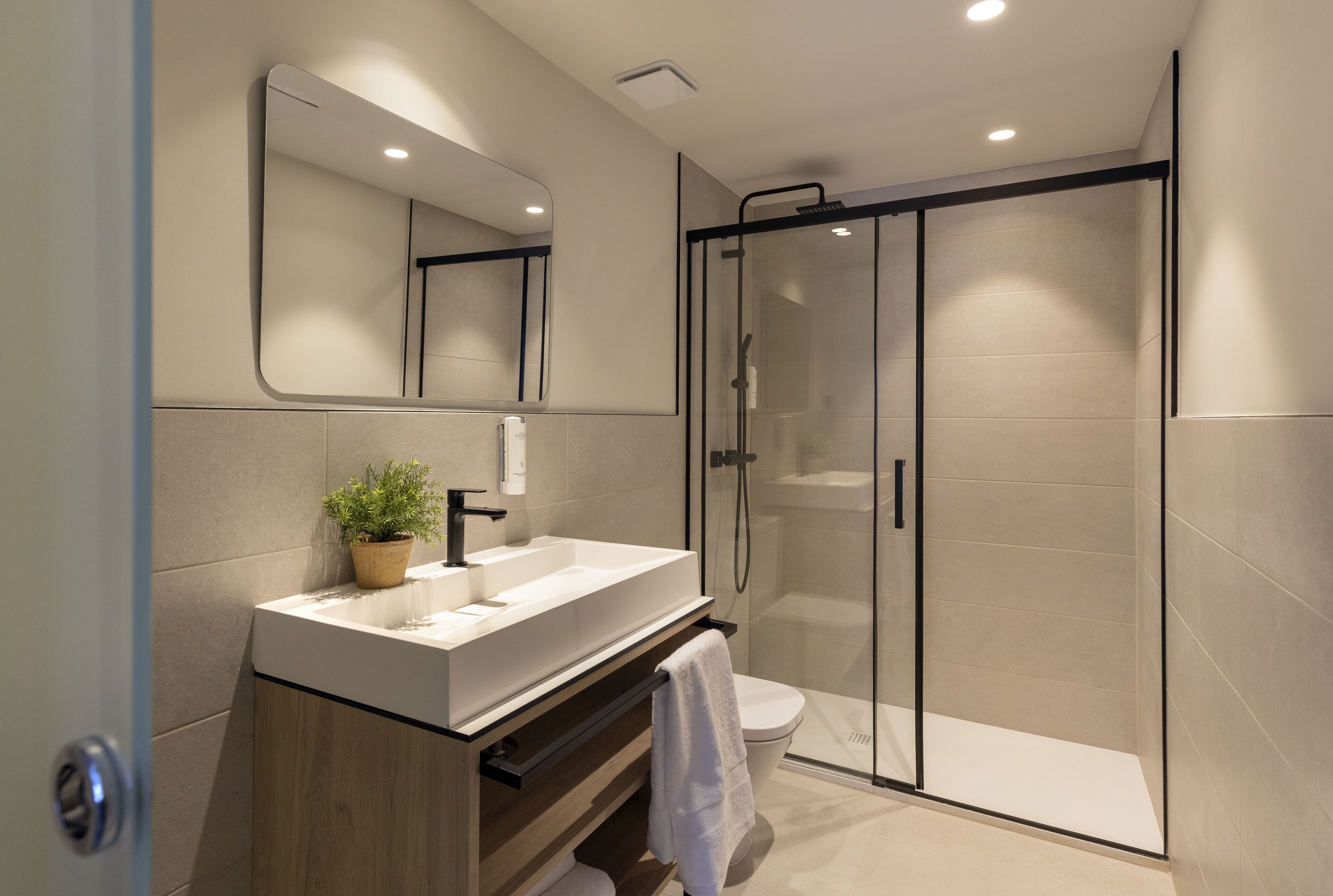 A modern bathroom with a glass-enclosed shower, a large mirror, and a wooden vanity.