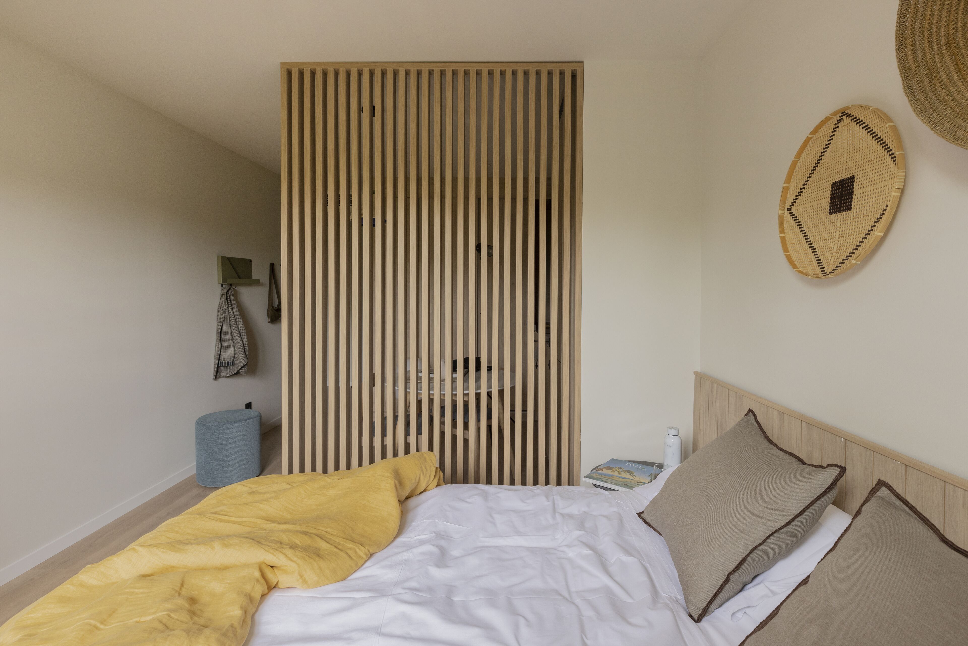 Ein Schlafzimmer mit einem Bett, einem Nachttisch, einer Lampe, einem Wandregal und einem gewebten Wandbehang.