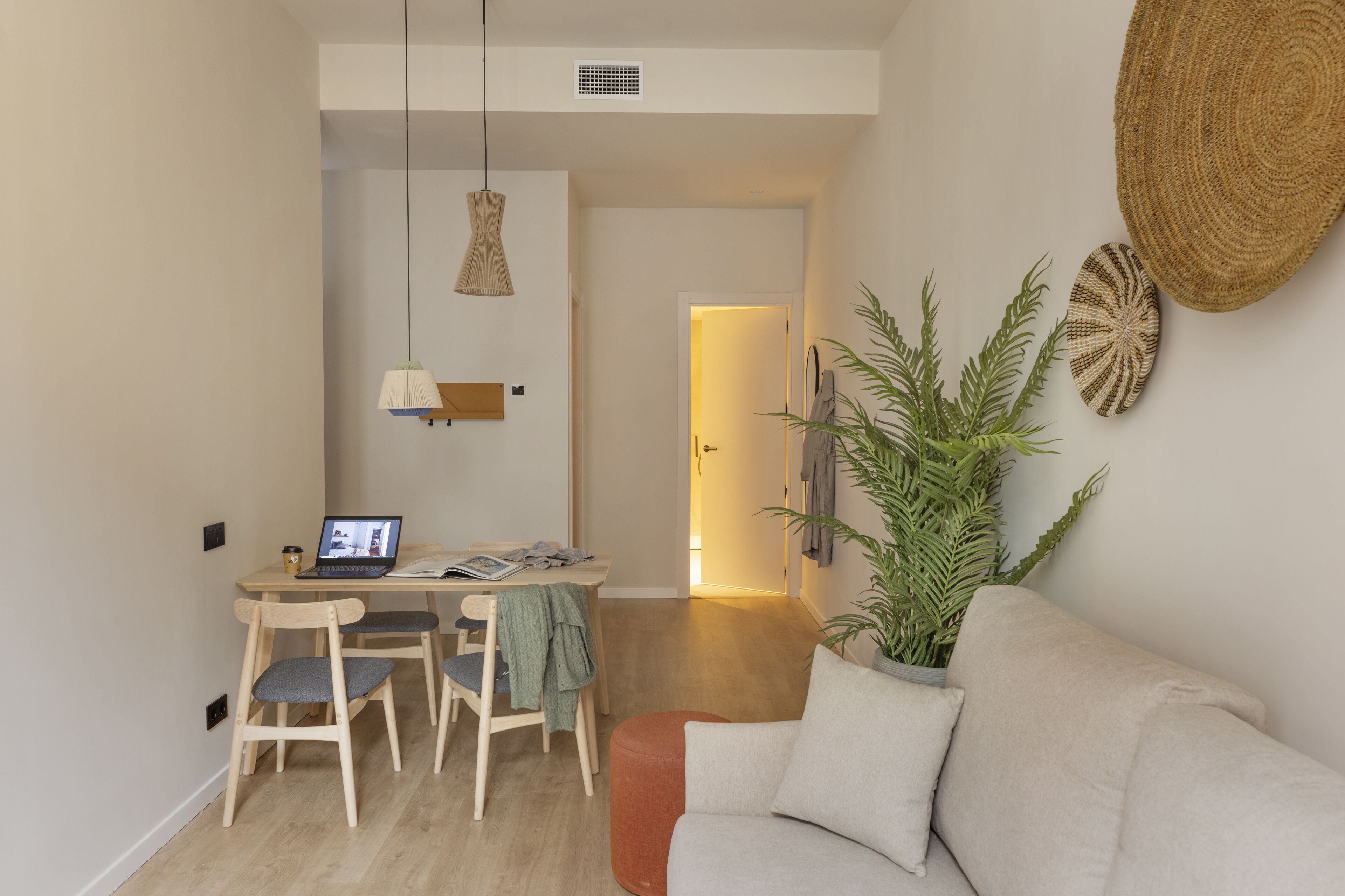 Un salon moderne avec un canapé, une table à manger et des chaises, un ordinateur portable et une plante en pot.