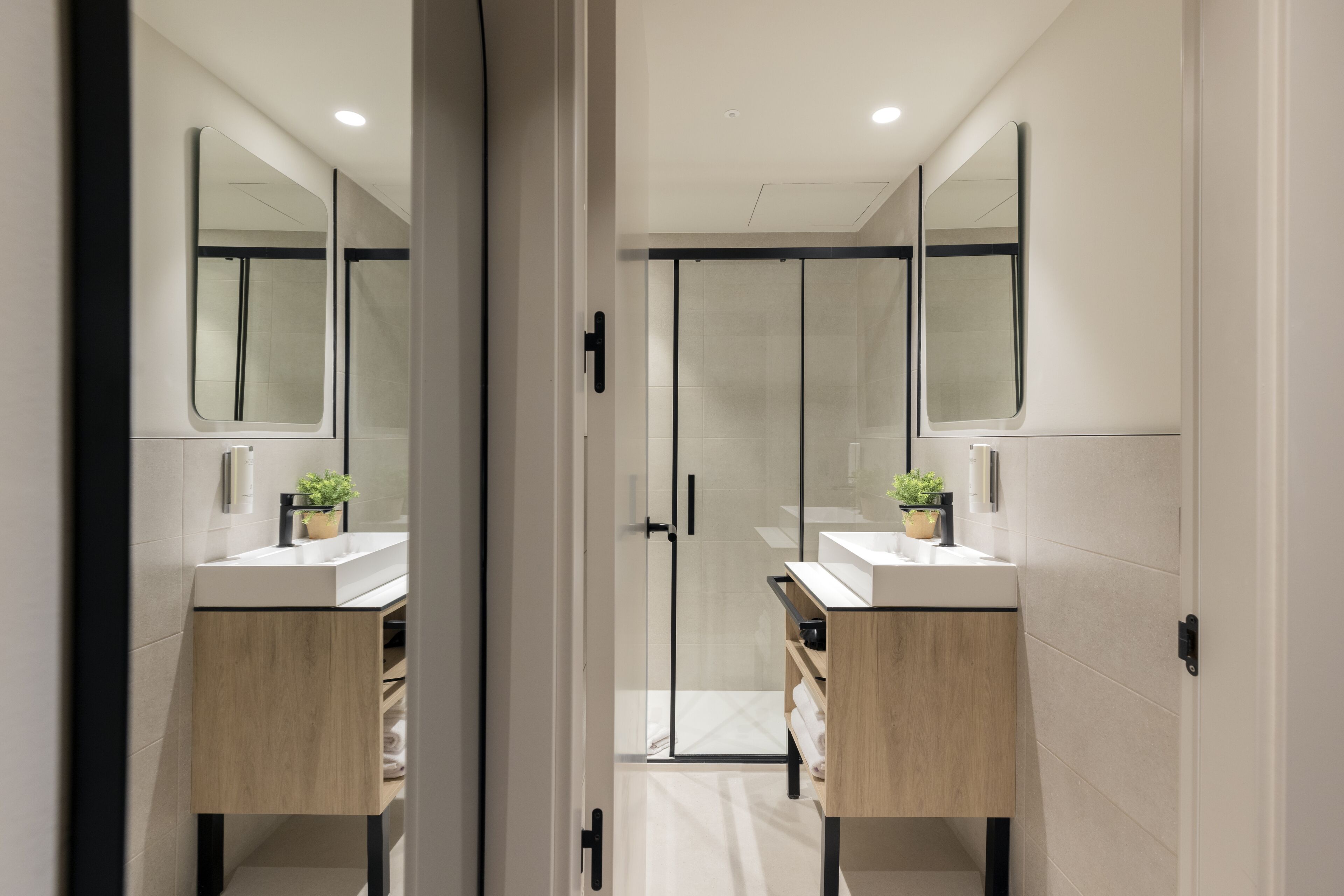 A modern bathroom with two sinks, a glass shower enclosure, and a large mirror.