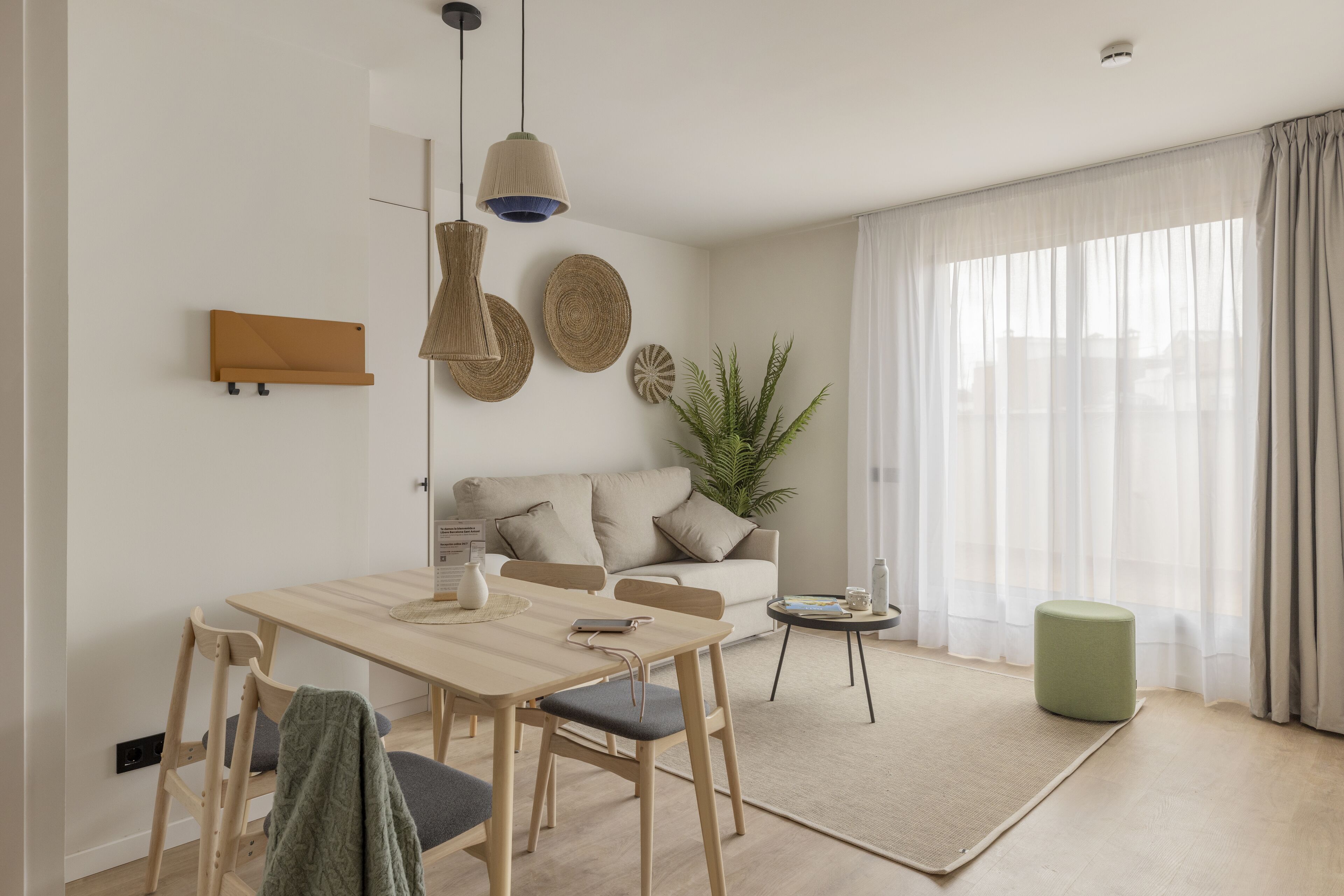A modern living room with a wooden dining table, a sofa, and a green ottoman.