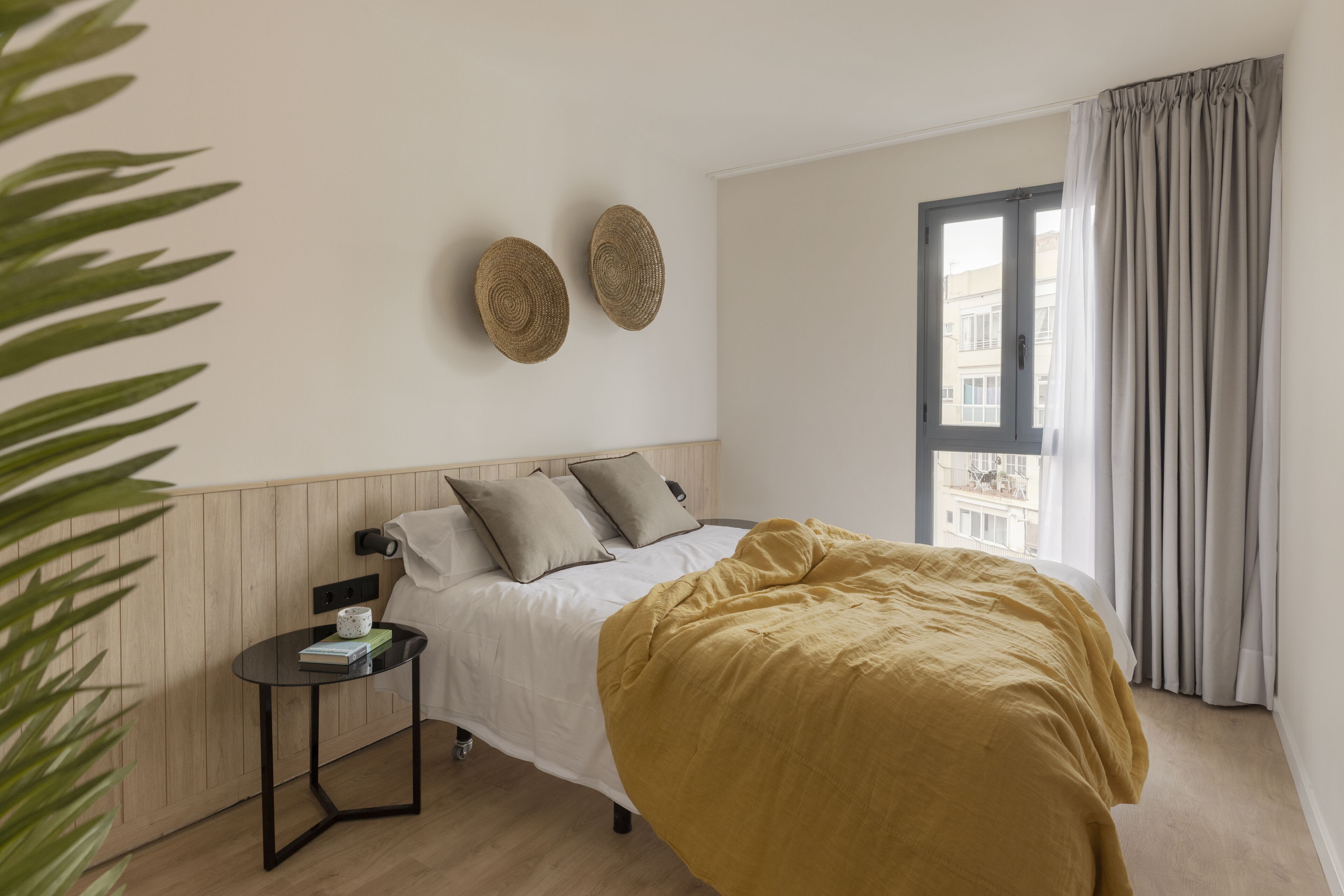 A modern bedroom with a bed, bedside table, and a view of the city through a window.