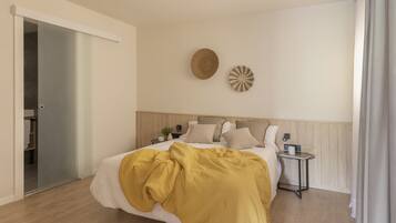 Un dormitorio con cama, mesitas de noche, un reloj en la pared y una puerta que da al baño.