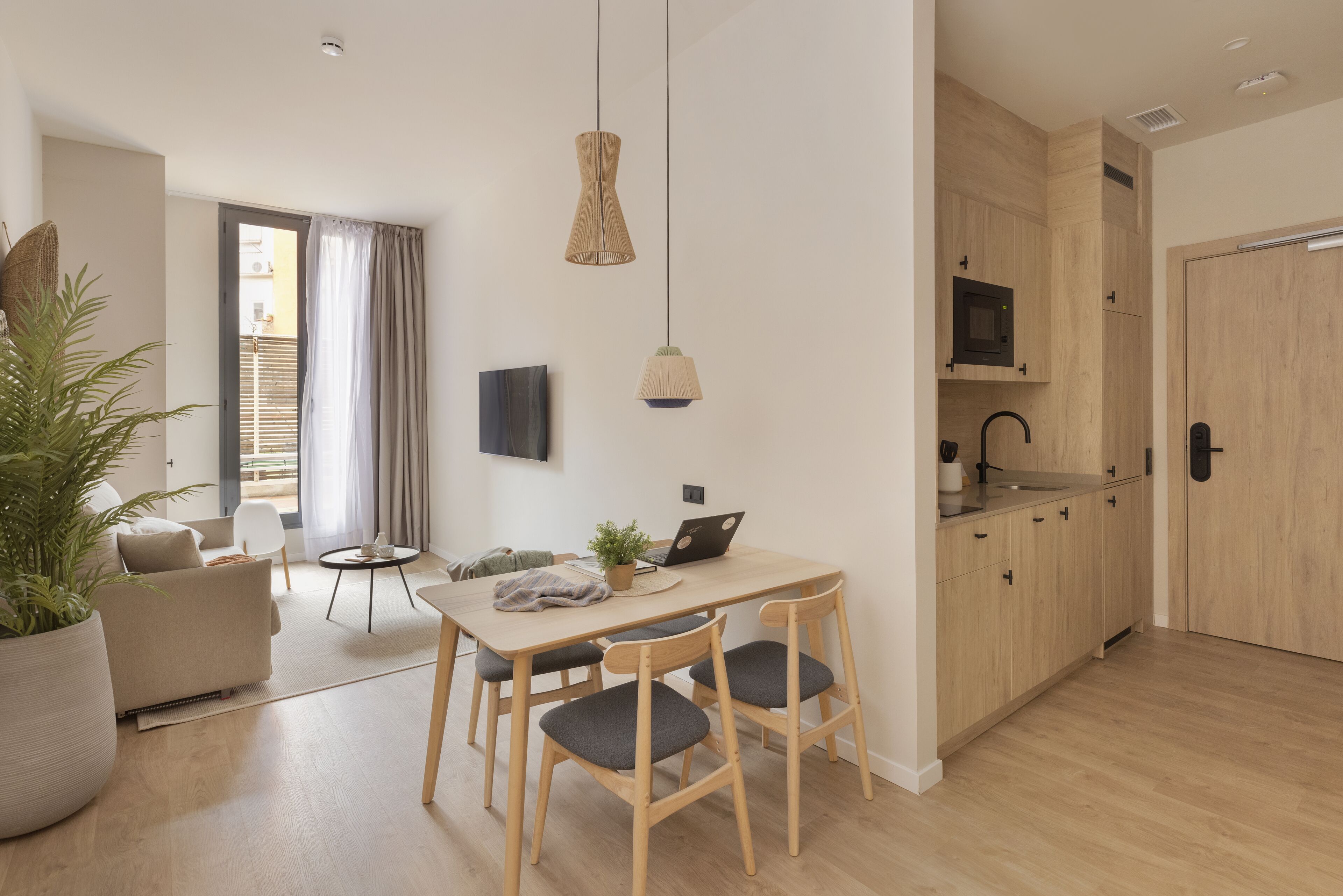 A modern kitchen with wooden cabinets, a dining table with chairs, a potted plant, and a laptop on the table.