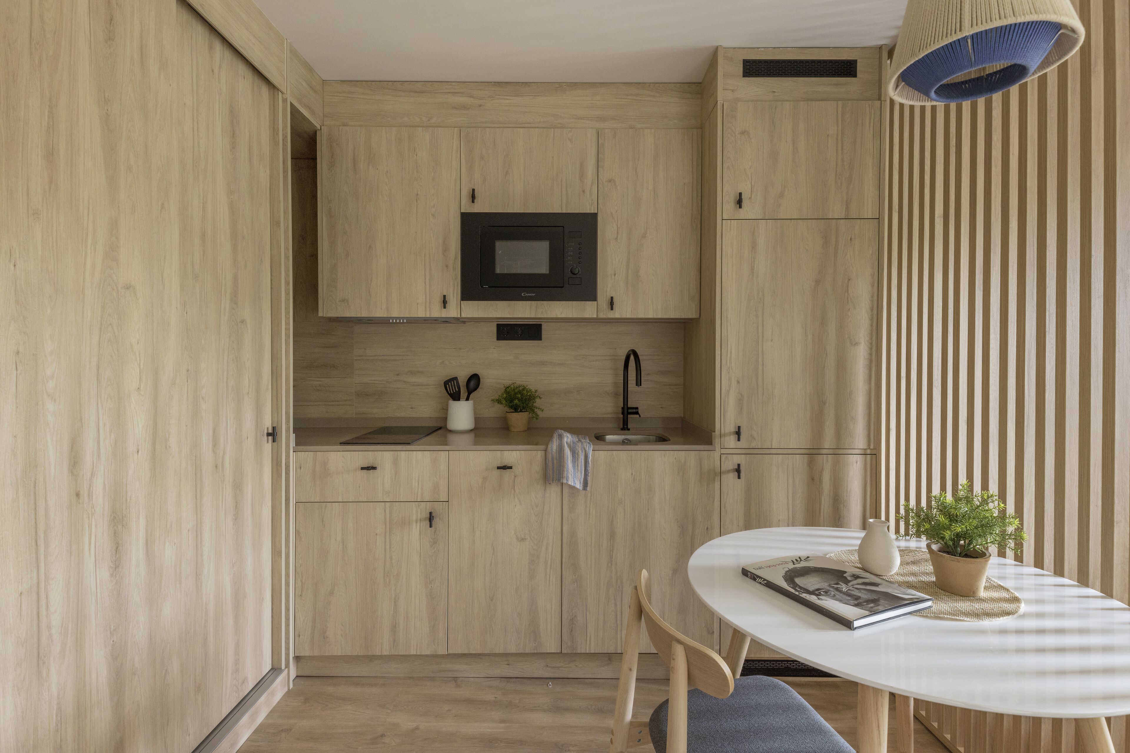 Una cocina moderna con armarios de madera, microondas, pileta y mesa de comedor con sillas.