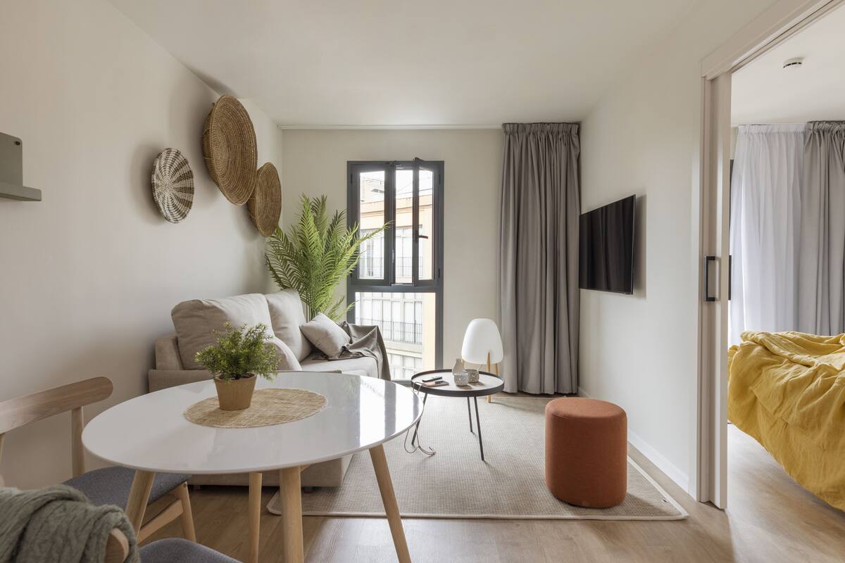 Un salon moderne avec un canapé, une table ronde agrémentée d’une plante, une petite table d’appoint et un lit jaune.