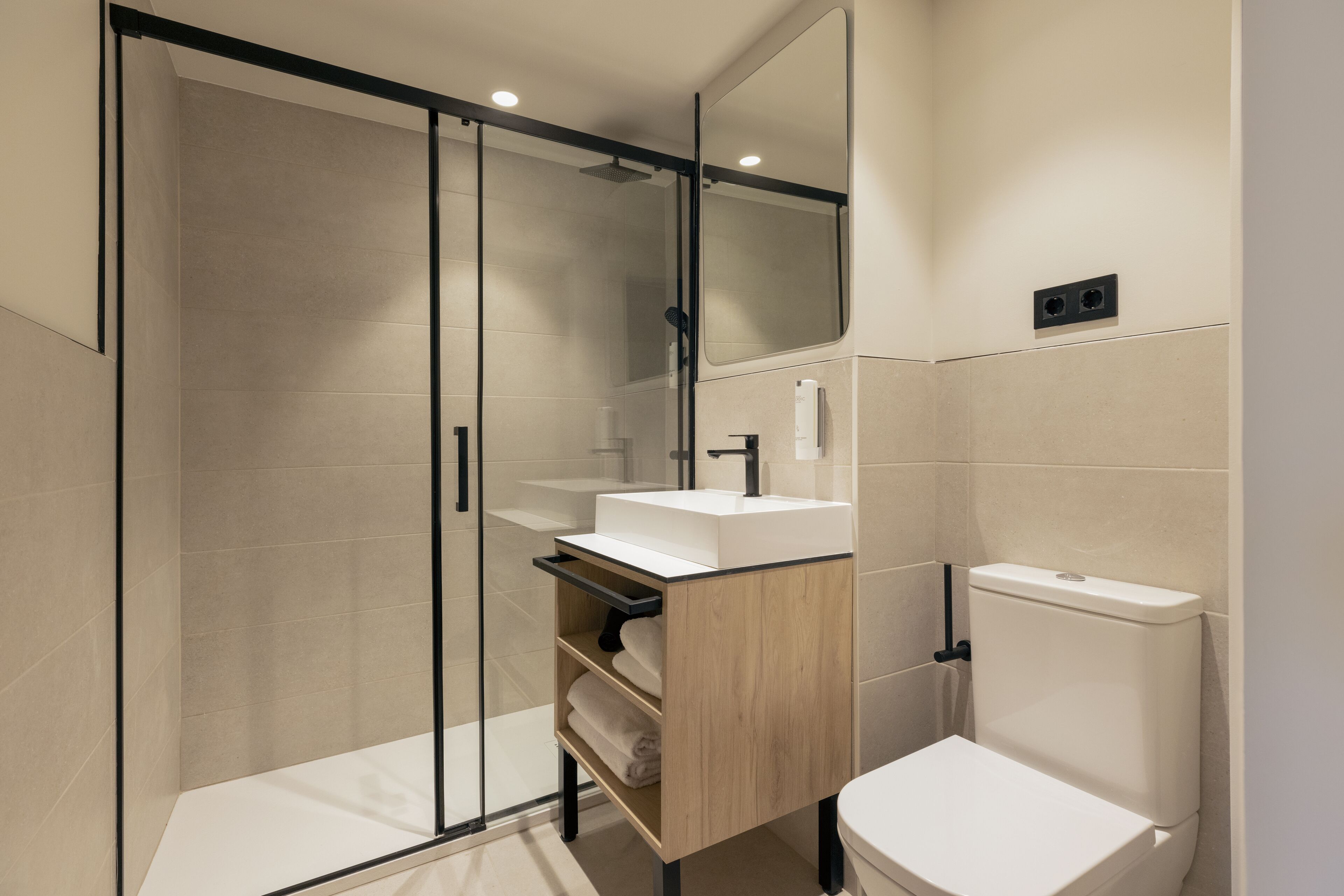 Un baño moderno con cabina de ducha de vidrio, tocador de madera con lavabo e inodoro.