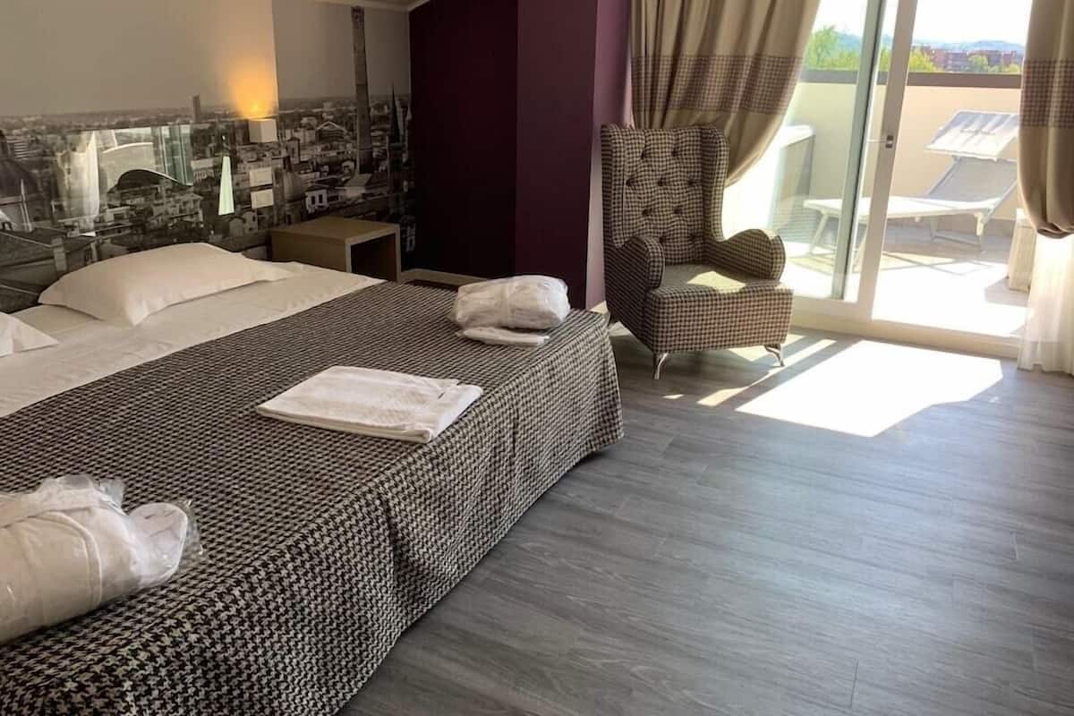 A hotel room with a large bed, a chair, and a view of the city through the window.