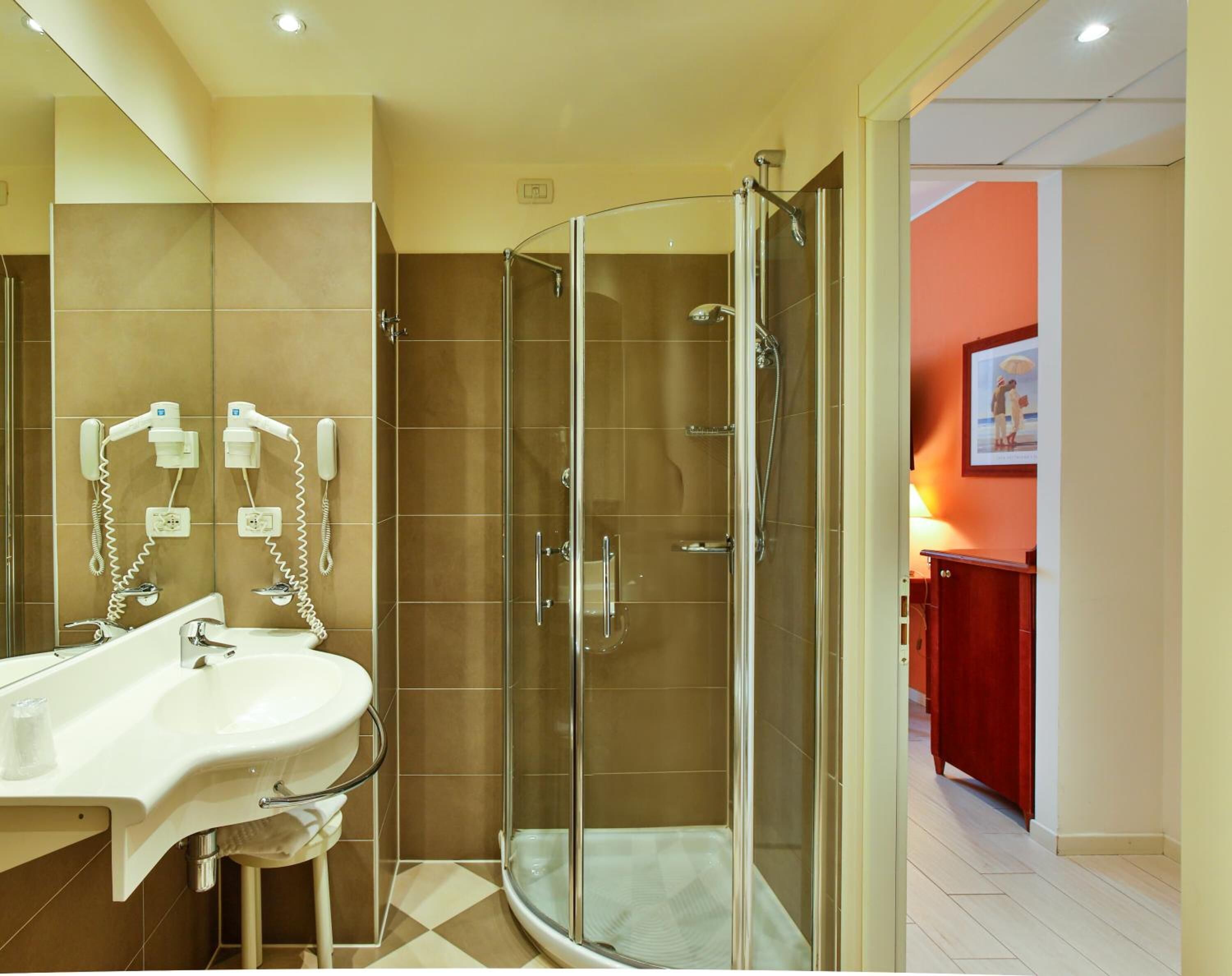 Un baño moderno con ducha de vidrio, lavamanos con espejo y teléfono.