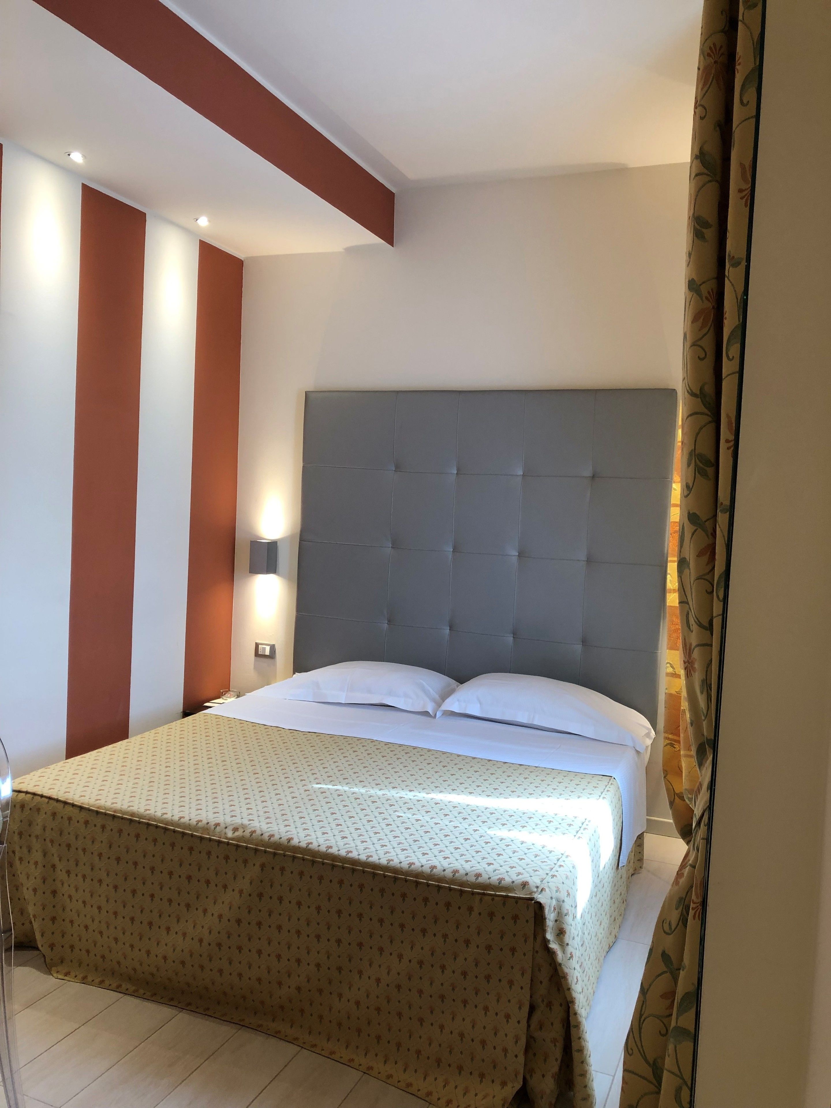 Een net opgemaakt bed met een bedspreide met een patroon, een gestuwd hoofdeinde en een muur met verticale strepen.