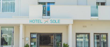 Un hotel llamado "HOTEL SOLE" con una fachada moderna, grandes puertas de vidrio y un área de estar al aire libre.