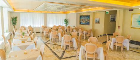 A banquet hall with multiple tables and chairs, a patterned floor, and a ceiling with recessed lighting.