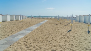 A beach with rows of white beach huts and a paved walkway.