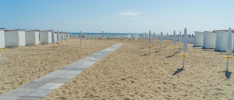 Una playa con hileras de cabañas blancas y un paseo marítimo empedrado.