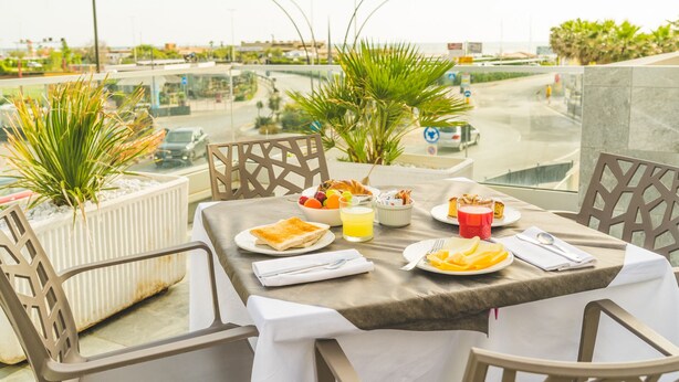 A balcony table with breakfast items, chairs, and potted plants.