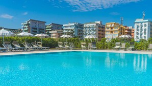 A swimming pool with lounge chairs and umbrellas, surrounded by multi-story buildings with balconies.