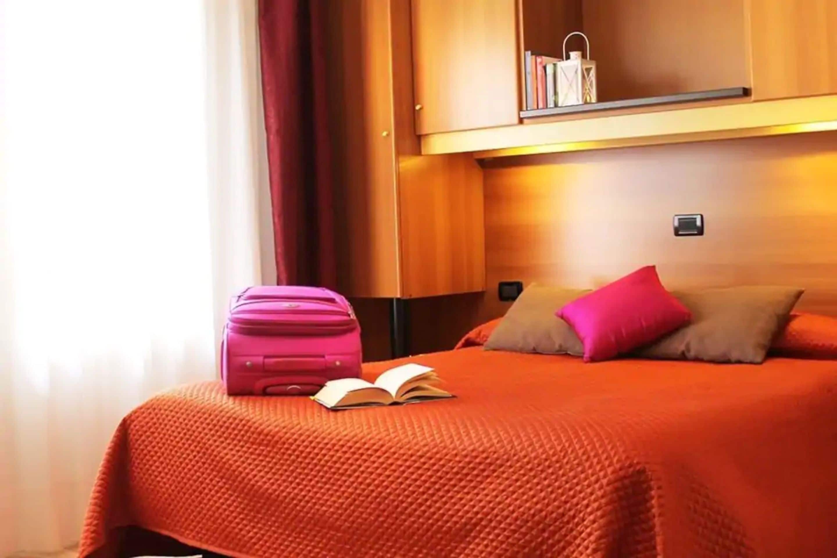 A hotel room with a bed, a suitcase, and a book.