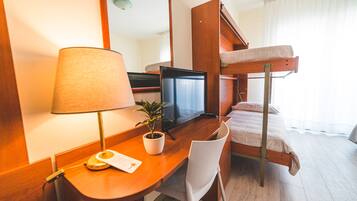 A hotel room with a wooden desk, a television, a bunk bed, a chair, and a potted plant.