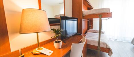 A hotel room with a wooden desk, a television, a bunk bed, a chair, and a potted plant.