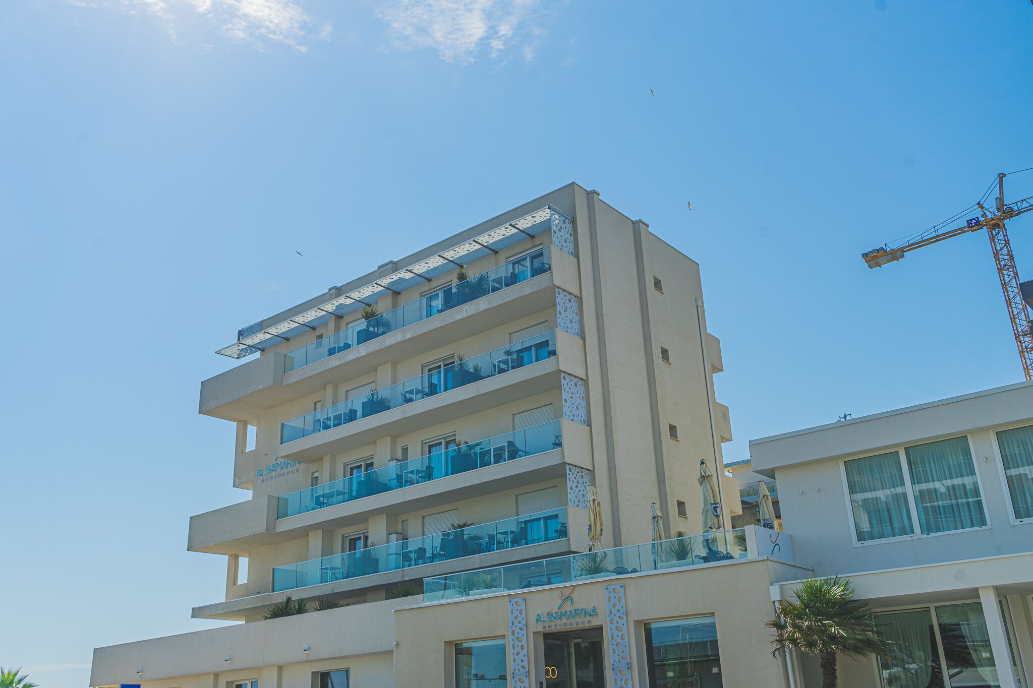 Un hotel de varios pisos con balcones, una grúa al fondo y cielo despejado.