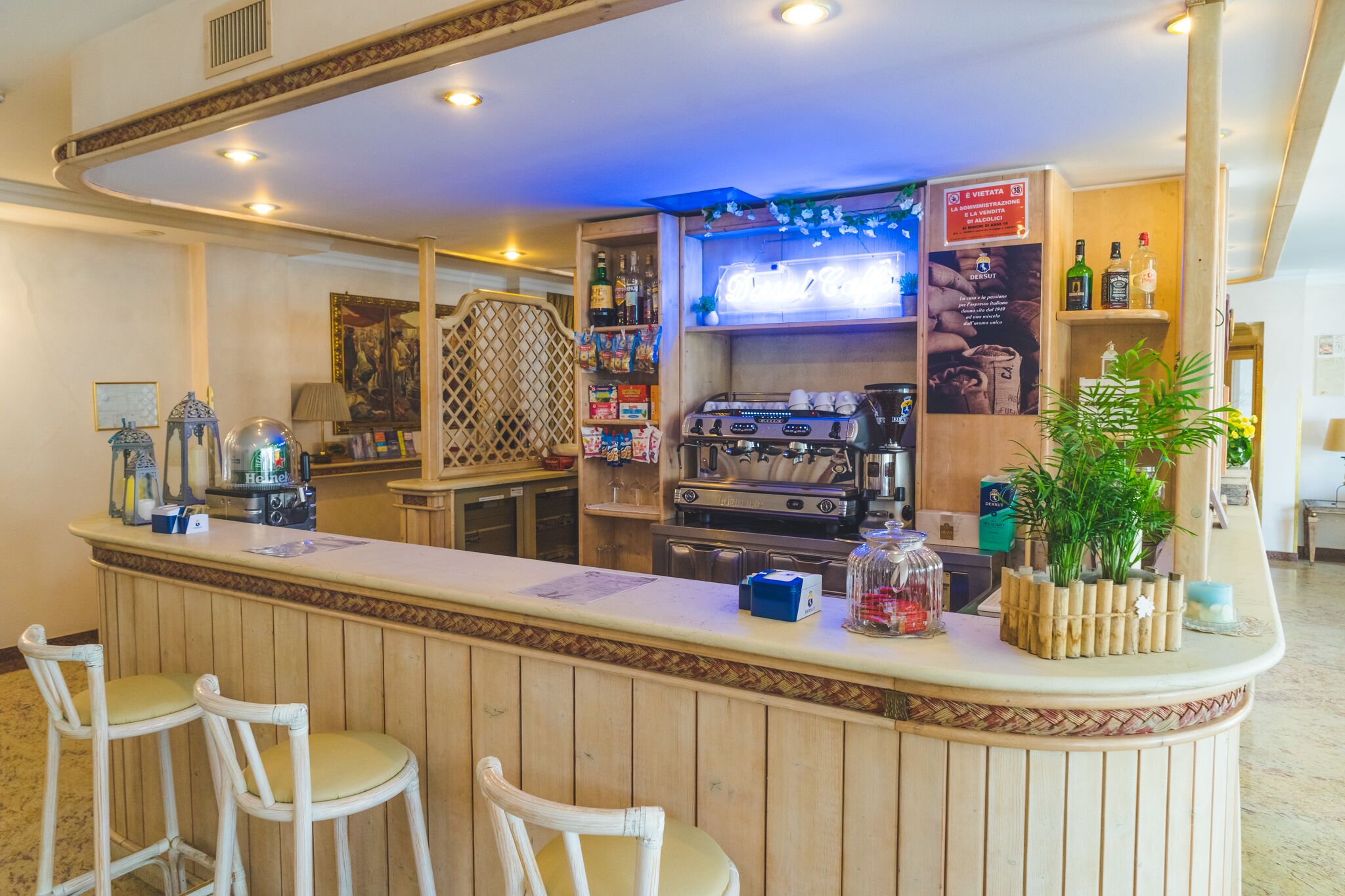A bar area with wooden bar stools, a coffee machine, and shelves with bottles and snacks.