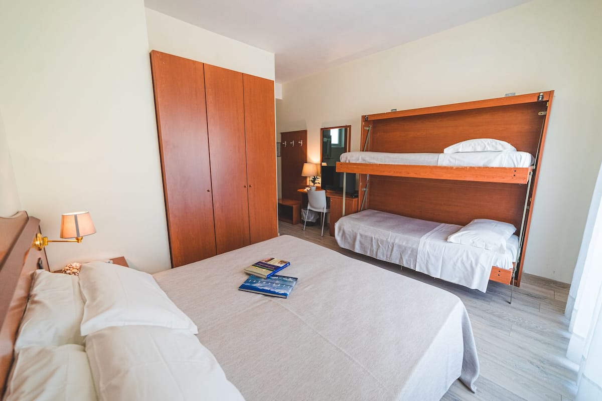 A hotel room with a bunk bed, a desk with a lamp, and a wardrobe.
