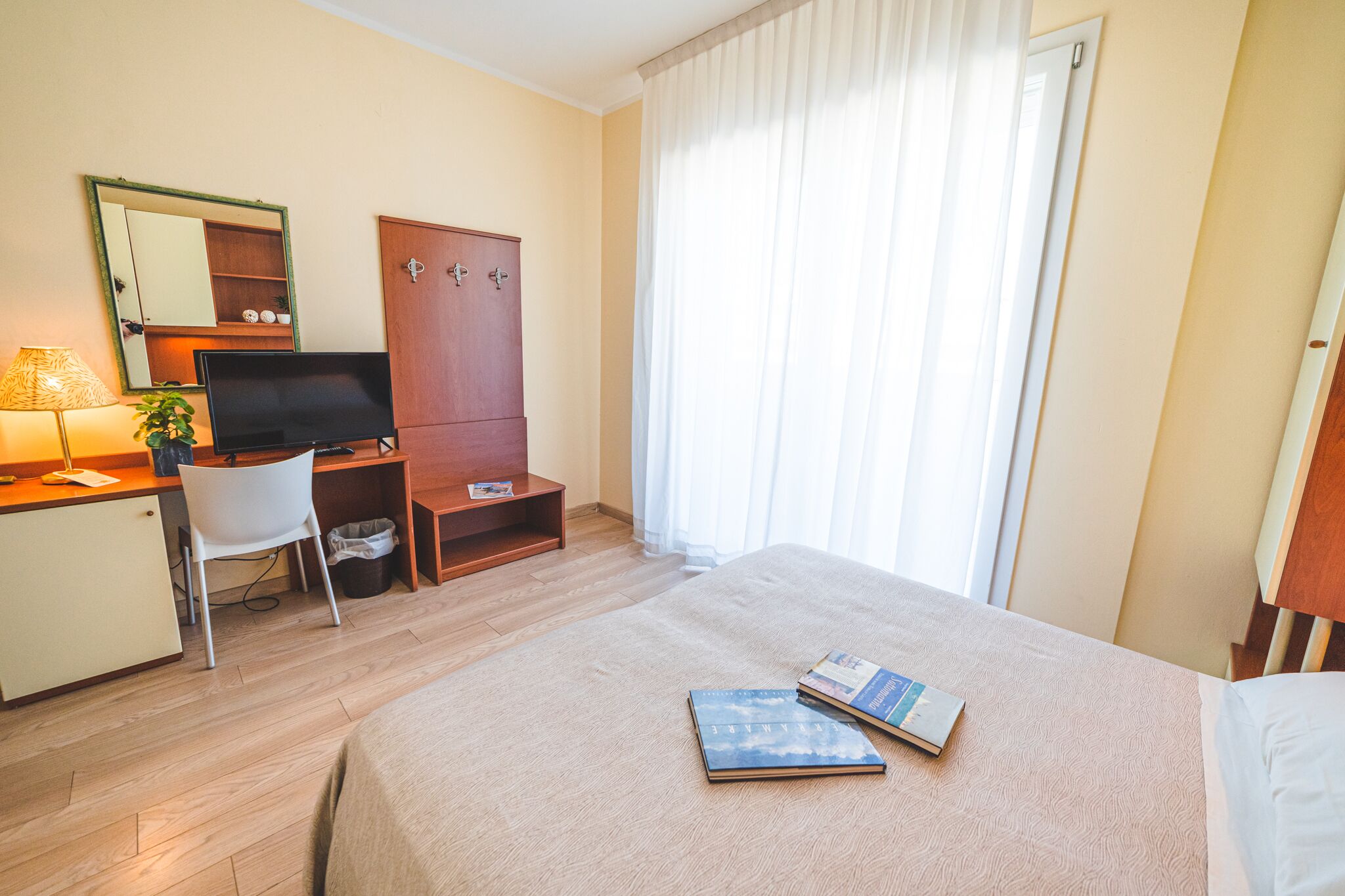 A hotel room with a bed, a desk with a computer, a mirror, and a wardrobe.