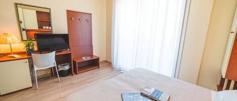 A hotel room with a bed, a desk with a computer, a mirror, and a wardrobe.