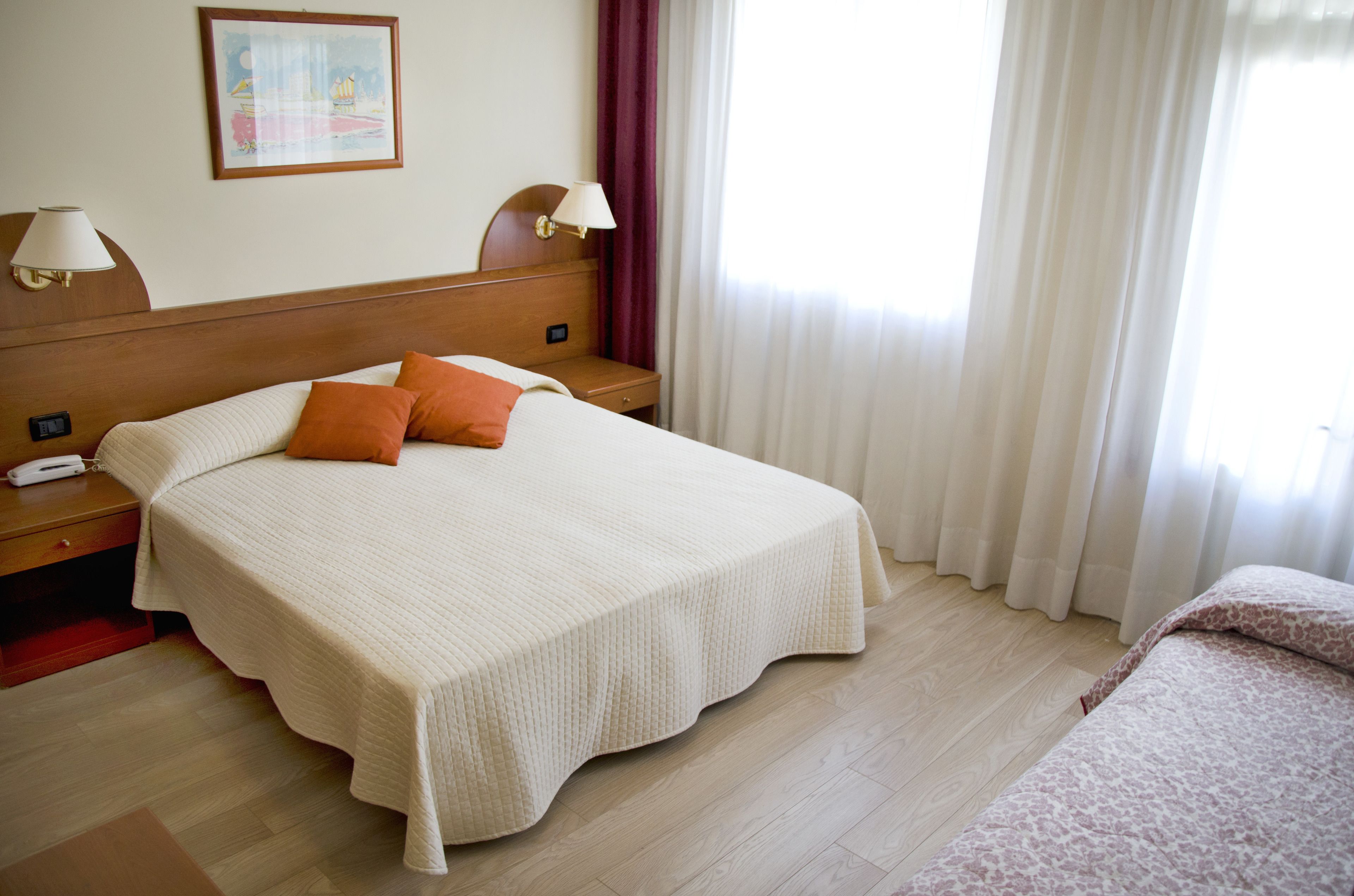A hotel room with a large bed, two bedside tables, a nightstand, a lamp, and a painting on the wall.