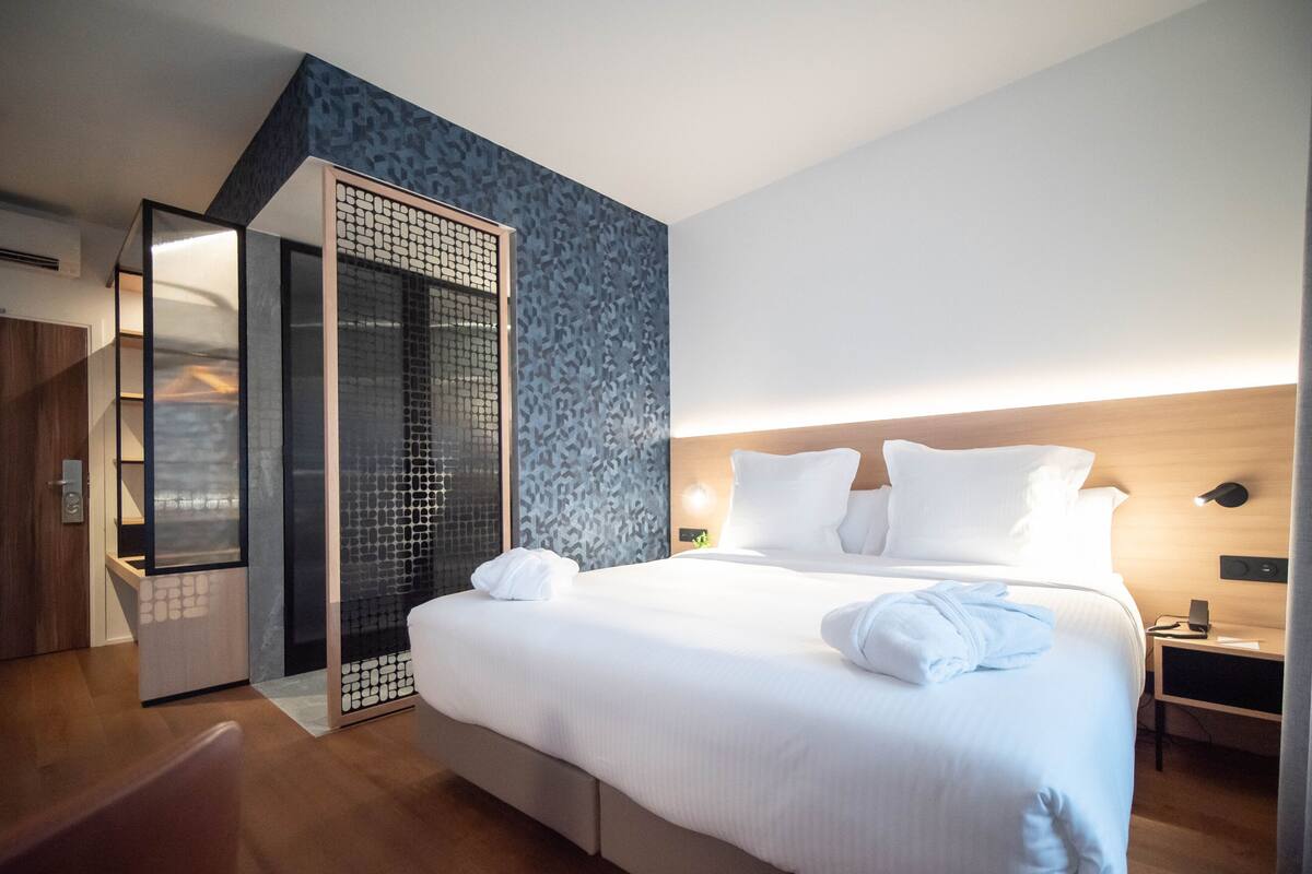 A modern hotel room with a large bed, a walk-in closet, and a patterned wall.
