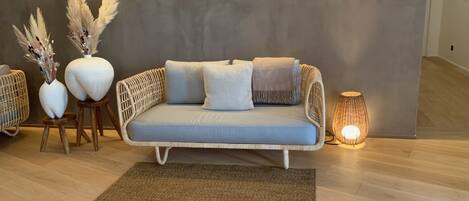 A modern living room with a light blue sofa, two white vases with pampas grass, a woven side table, a brown rug, and a lit floor lamp.