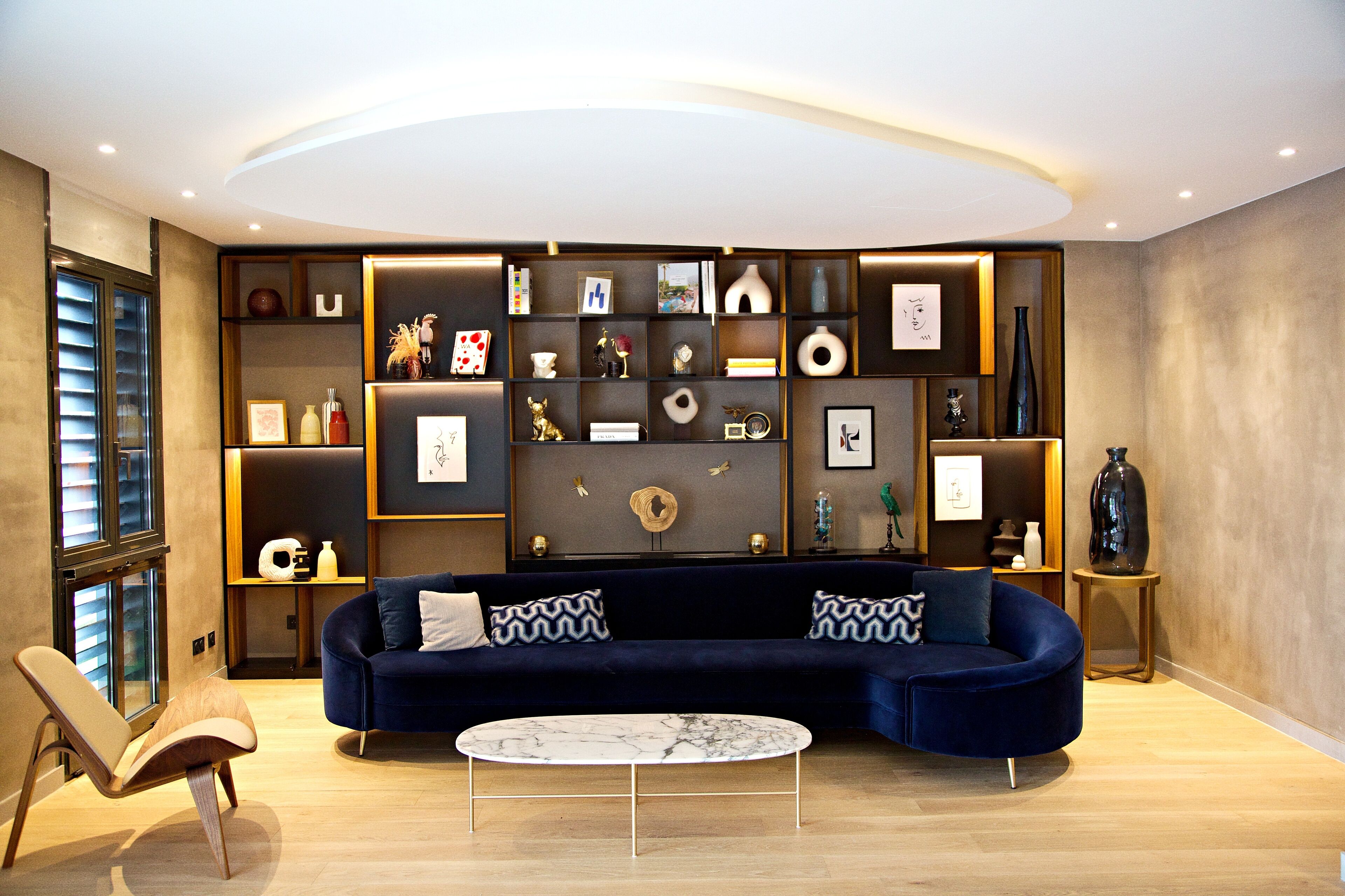 A modern living room with a dark blue sofa, a round coffee table, and a built-in shelving unit with various decorative items.