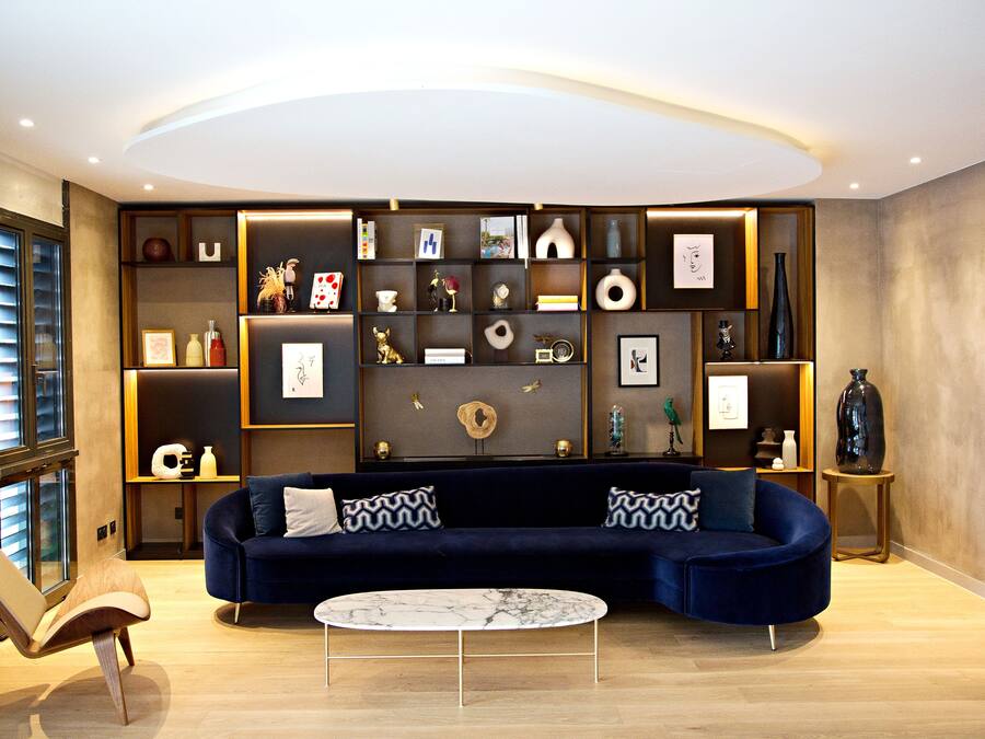 A modern living room with a dark blue sofa, a round coffee table, and a built-in shelving unit with various decorative items.