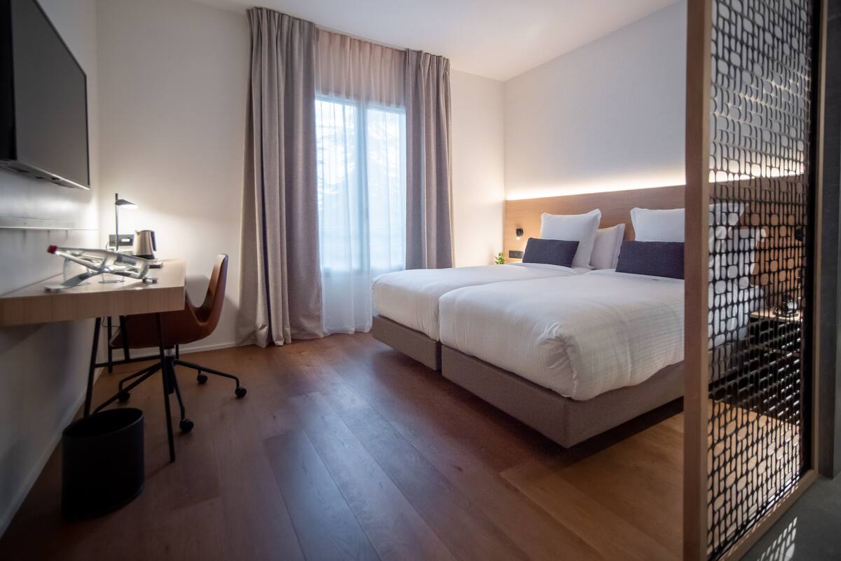 A modern hotel room with a large bed, a desk with a chair, and a TV mounted on the wall.