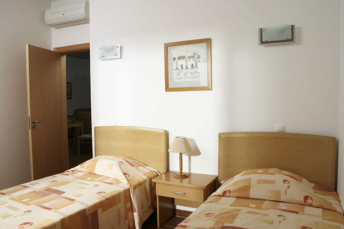 A hotel room with two beds, a nightstand, a lamp, and a framed picture on the wall.