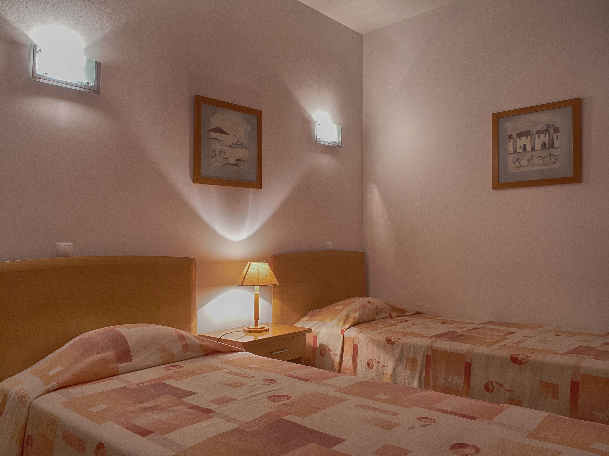 Une chambre d’hôtel avec deux lits, une table de chevet avec une lampe et deux appliques murales.