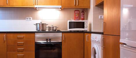 A kitchen with wooden cabinets, a stove, microwave, oven, and washing machine.
