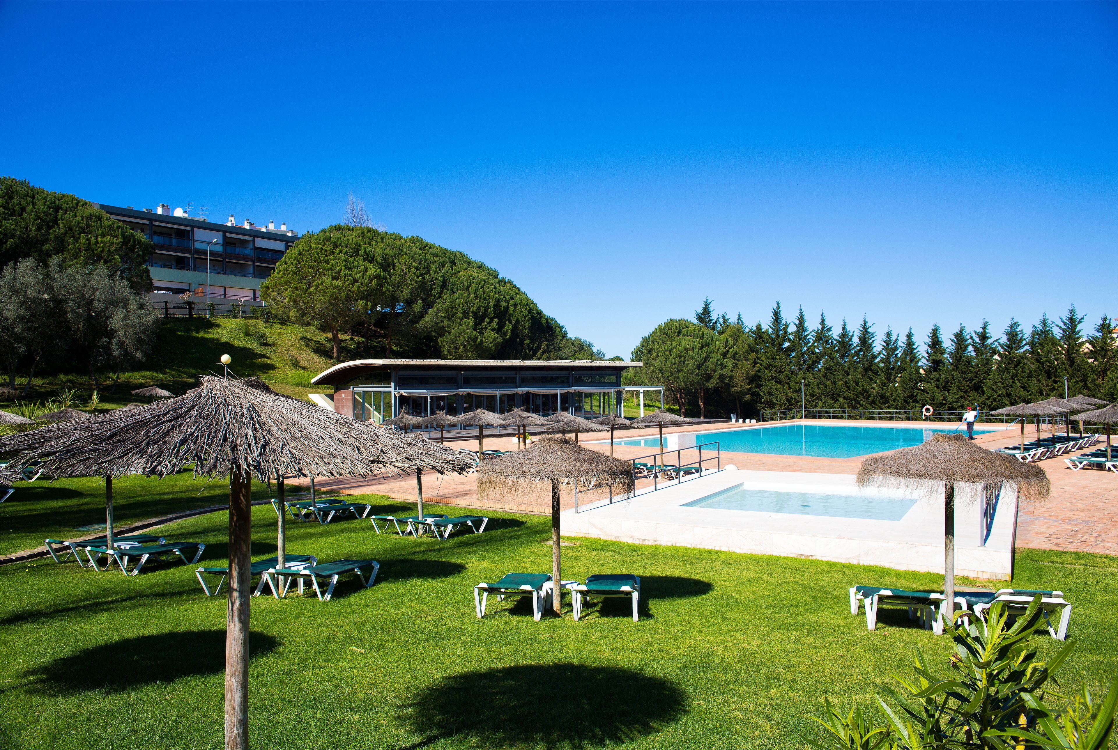 A poolside area with lounge chairs, umbrellas, and a building in the background.