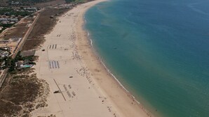 An aerial view of a beach with a long stretch of sand, a few umbrellas, and a clear blue sea. - Vitasol Park (Lagos)