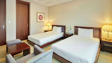 A hotel room with two single beds, a sofa, a small table, and a nightstand with a lamp.