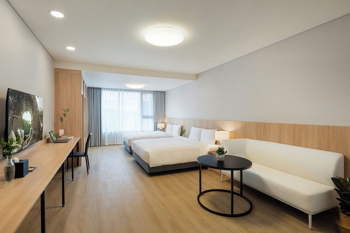 Una habitación de hotel moderna con cama, sofá, escritorio con computadora y mesa de comedor.