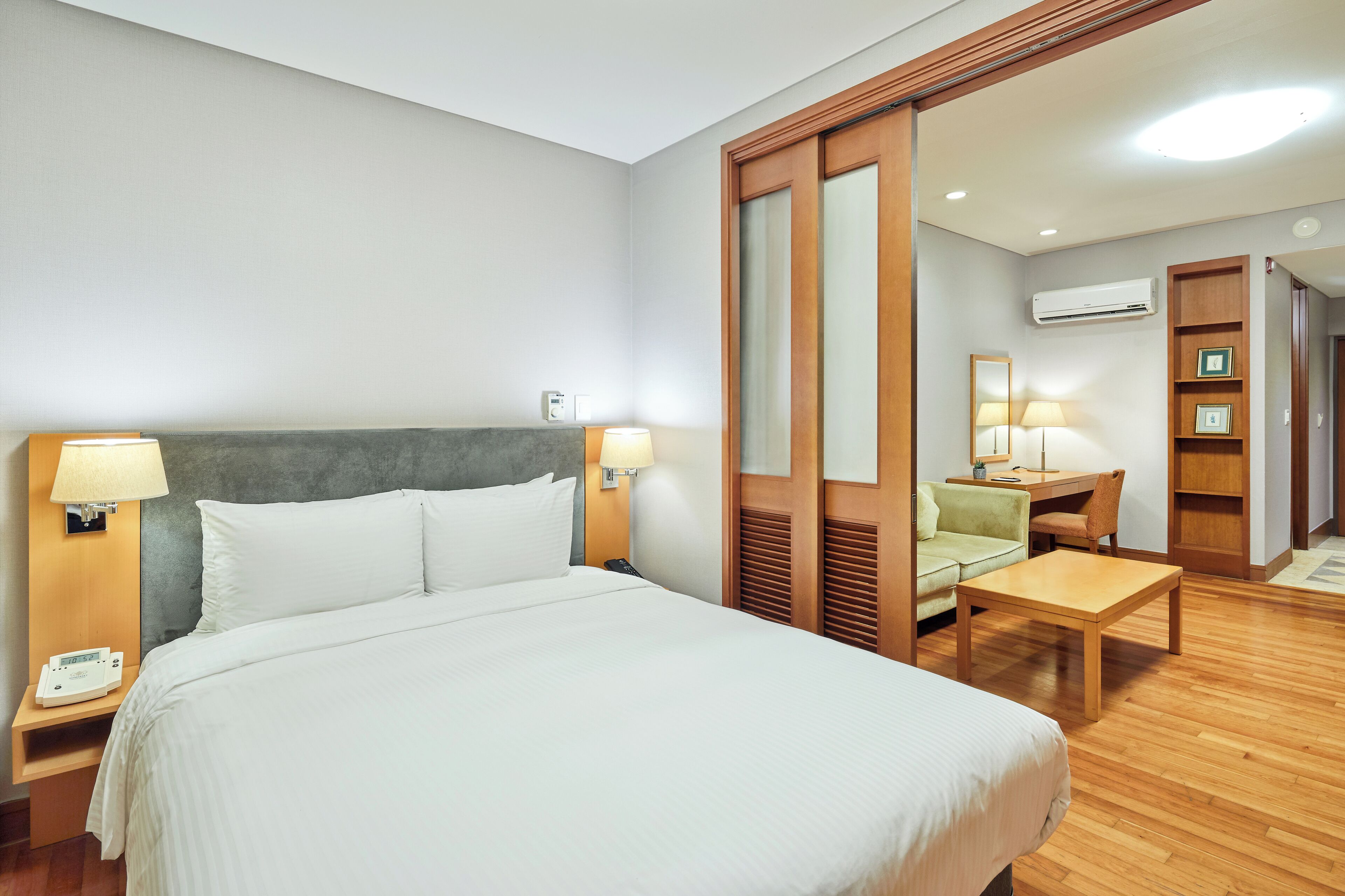 A hotel room with a large bed, bedside tables with lamps, a desk, a chair, and a wardrobe.