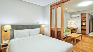 A hotel room with a large bed, bedside tables with lamps, a desk, a chair, and a wardrobe.