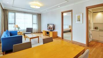 A hotel room with a dining area, a sofa, a TV, a bed, a kitchen, and a bathroom.