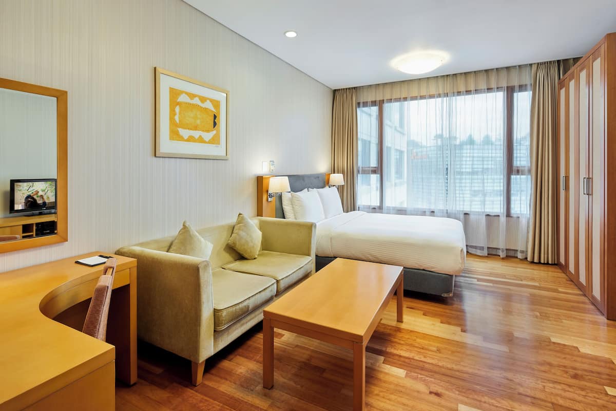 Habitación de hotel con cama, sofá, escritorio y un ventanal grande.