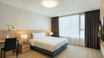 A hotel room with a bed, bedside tables, a desk, a chair, and a large window with curtains.