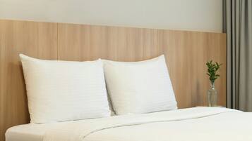 A hotel room with a wooden headboard, two white pillows, a bed with white bedding, and a small potted plant on the nightstand.
