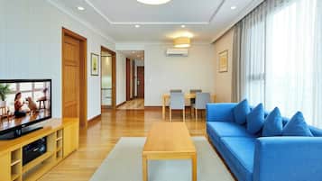 A modern living room with a wooden coffee table, a blue sofa with cushions, a television, and a dining area with a table and chairs.